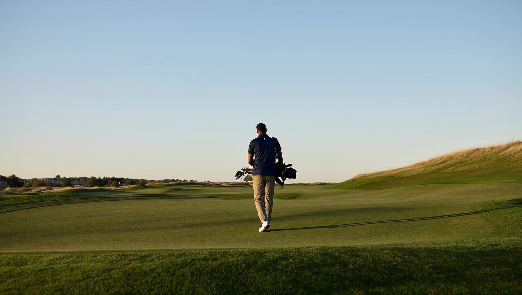 A golfer walking a links fairway toward the green under an open sky